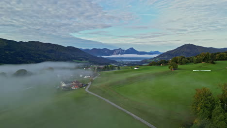 Nube-De-Niebla-Ligera-Sobre-El-Pueblo-En-Campos-Verdes-Del-Valle-De-Montaña-Alpino