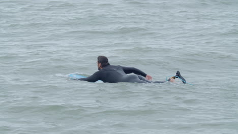 Hombre-Deportivo-En-Traje-De-Neopreno-Con-Pierna-Artificial-Acostado-En-La-Tabla-De-Surf-Y-Nadando-En-El-Océano-4