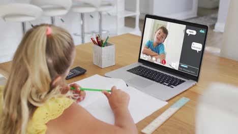 Schoolgirl-using-laptop-for-online-lesson-at-home,-with-boy-talking-and-web-chat-on-screen