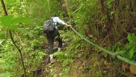 woman uses helpful rope on steep section of lush green jungle hike