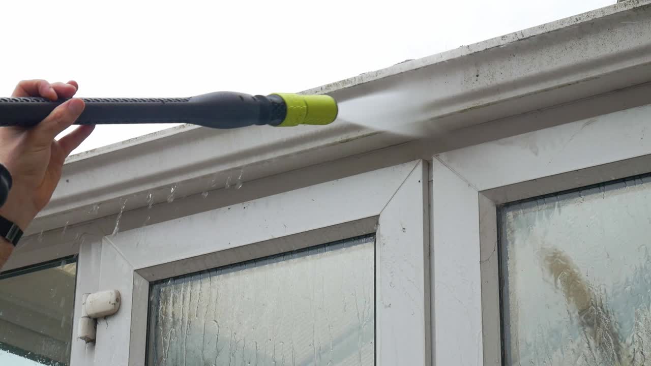 Power washing white gutters above conservatory french doors with a pressure washer