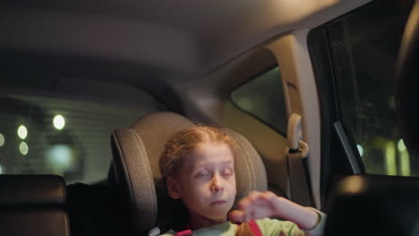 a close view of a child turning on the light in a car, reaching up towards the ceiling with focused intent, the background includes blurred lights from passer by car