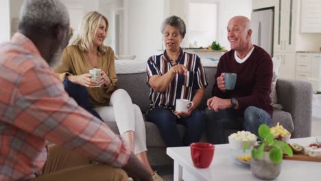 two diverse senior couples sitting on a couch drinking tea together at home