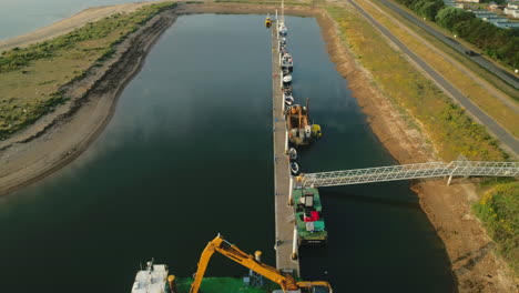 Drohnenaufnahme-Eines-Baggers-Mit-Kran-Auf-Einem-Boot-Und-Anderen-Booten-An-Einem-Kleinen-Dock-In-Wells-next-the-Sea-North-Norfolk-UK-Ostküste