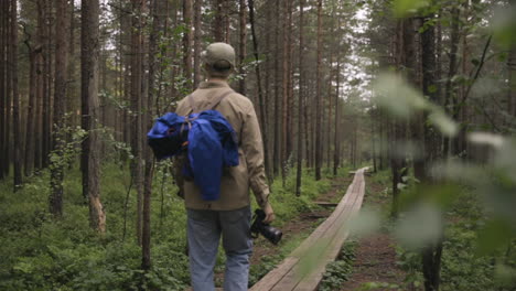 Photographer-walks-on-pathway-in-forest,-pan-from-behind-blurry-plant