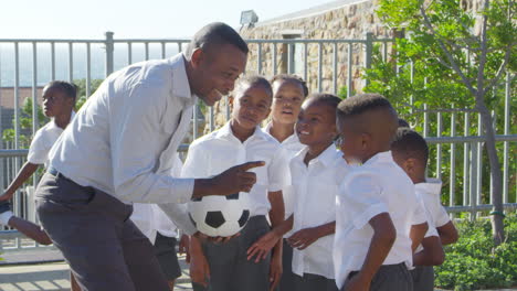 teacher holds ball and talks to school kids in playground