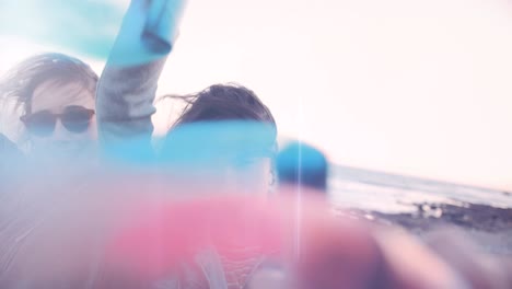 young hipster women celebrating with colorful smoke bombs at beach