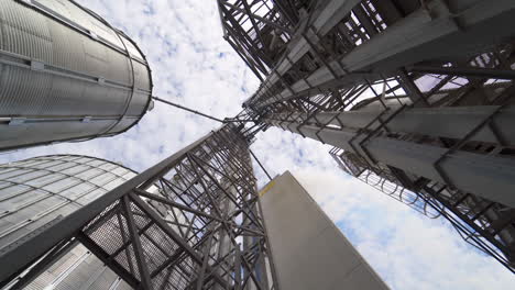metal towers on industrial plant. steel construction on a modern agricultural factory with grain elevators on sky background. view from below.