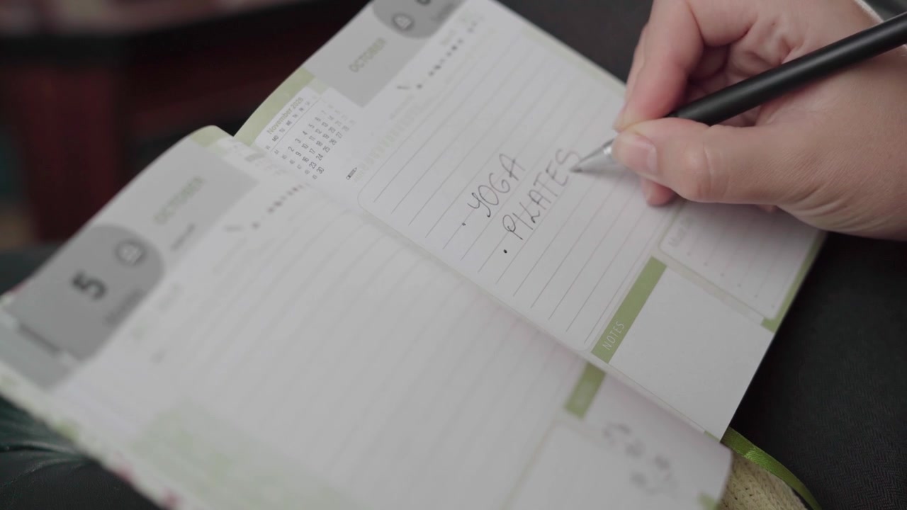 Woman notes yoga and pilates sessions in a dated weekly fitness planner, organizing her workout routine by hand.
