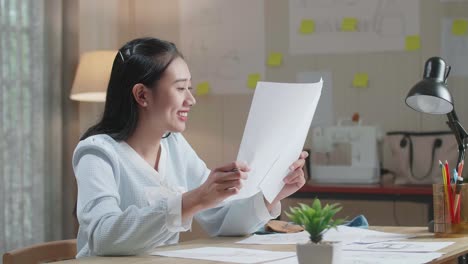 asian woman designer positively shaking her head while looking at the layout bond at the office