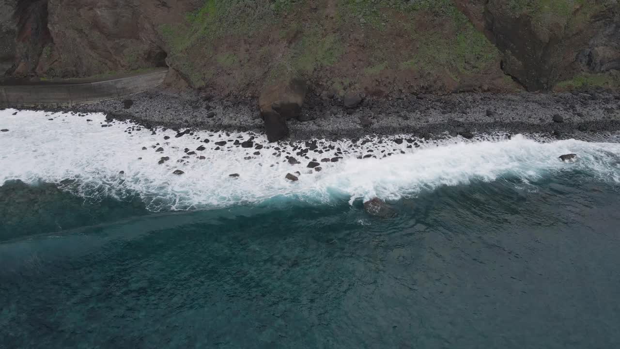 Aerial view of waves crushing into a pebble beach, turquoise water and white foam