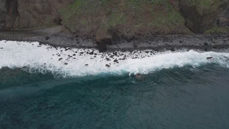 Aerial-view-of-waves-crushing-into-a-pebble-beach,-turquoise-water-and-white-foam