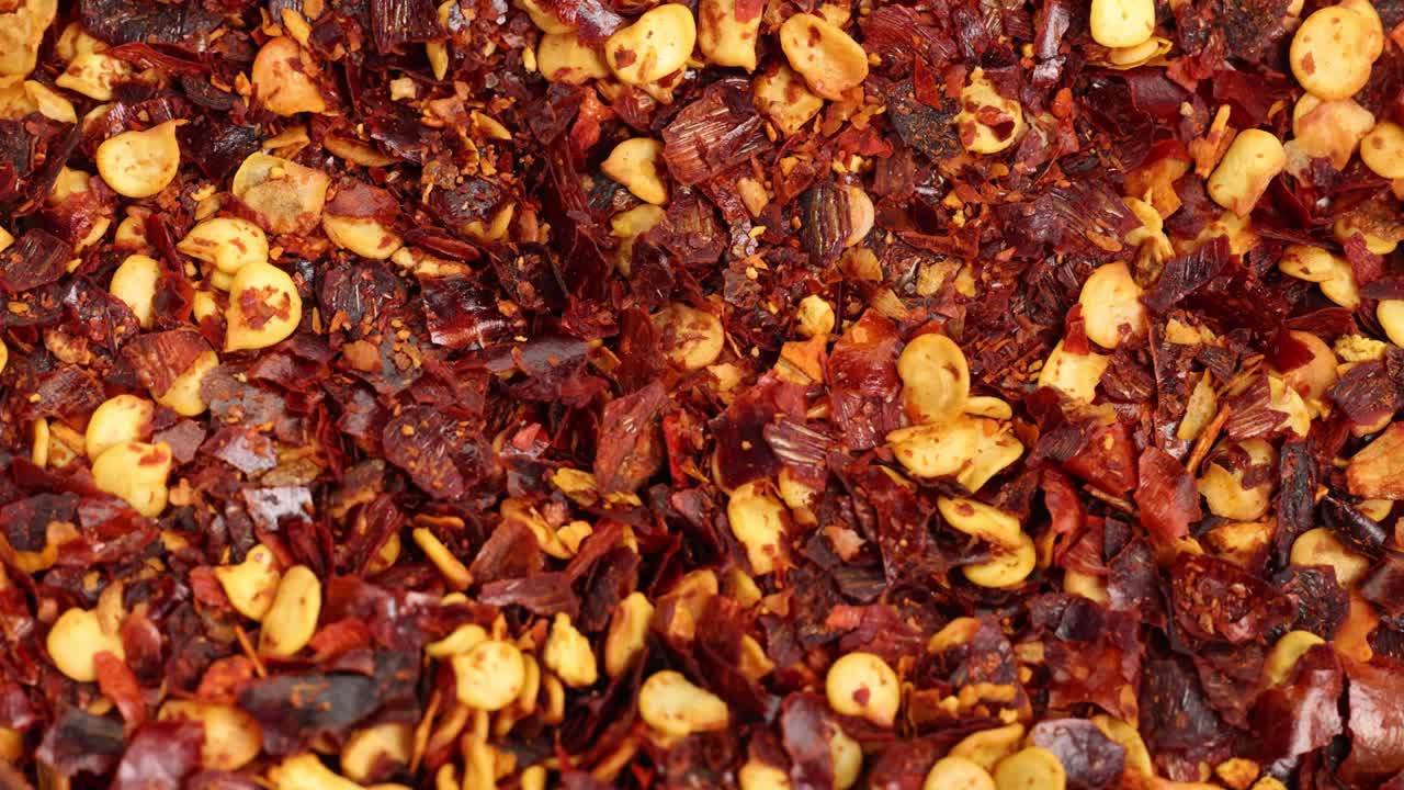 Macro view of chili flakes and seeds cascading, highlighting texture and vibrant colors under bright lighting
