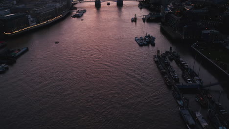 Aerial-view-of-water-surface-reflecting-colourful-twilight-sky.-Tilt-up-reveal-of-Tower-Bridge-and-Shard-skyscraper.-London,-UK