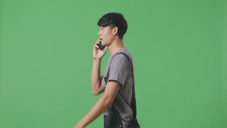 녹색 스크린 배경 스튜디오에서 는 동안 스마트폰으로 이야기하고 주변을 둘러보는 아시아 남성 노동자의 측면 시각