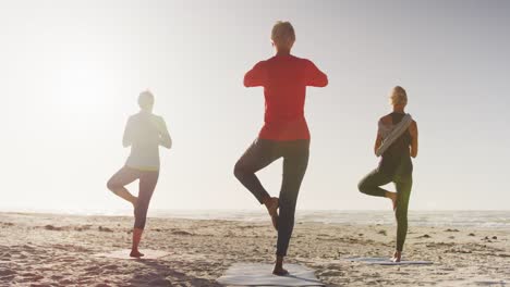 athletic women performing yoga in the beach