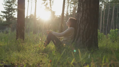 lady leans on tree trunk bark in forest at sunset. young woman rests in fresh air thinking about mental health improvement. coping with personal problems in nature