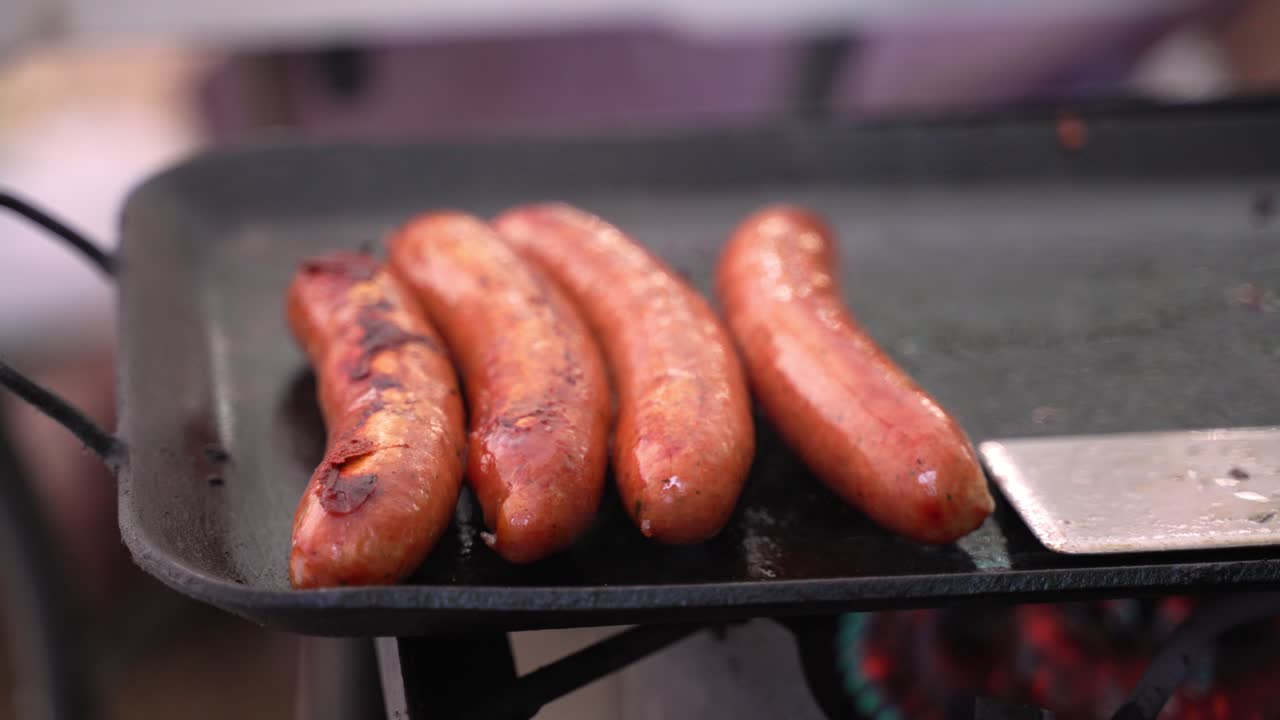 enlaces de salchichas carne de res de cerdo a la parrilla y ahumado en una parrilla de hierro fundido cocinada con propano en el campamento barbacoa al aire libre con personas en segundo plano durante el verano