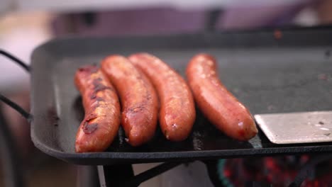 sausage links pork beef meat grilling and smoking on cast iron skillet grill cooked with propane at campsite outdoor barbecue with people in background during summer