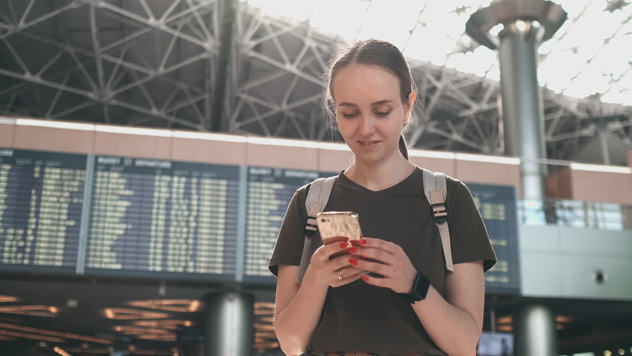 una viajera con una mochila está en el aeropuerto mirando la pantalla de su teléfono inteligente y escribiendo un mensaje. tarjeta de embarque electrónica para el tren de avión