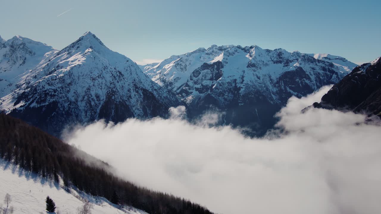 Bulutların arasından karlı bir dağ silsilesine doğru uçan drone videosu.