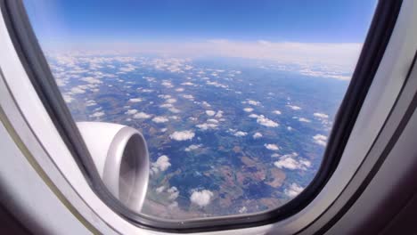 Mirando-Por-La-Ventana-De-Un-Avión-En-Las-Nubes-Y-El-Suelo,-Día-Soleado