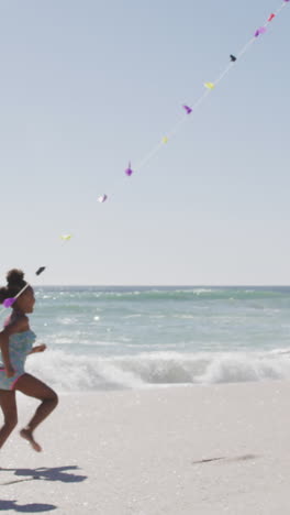 familia afroamericana sonriente corriendo y volando cometa en una playa soleada