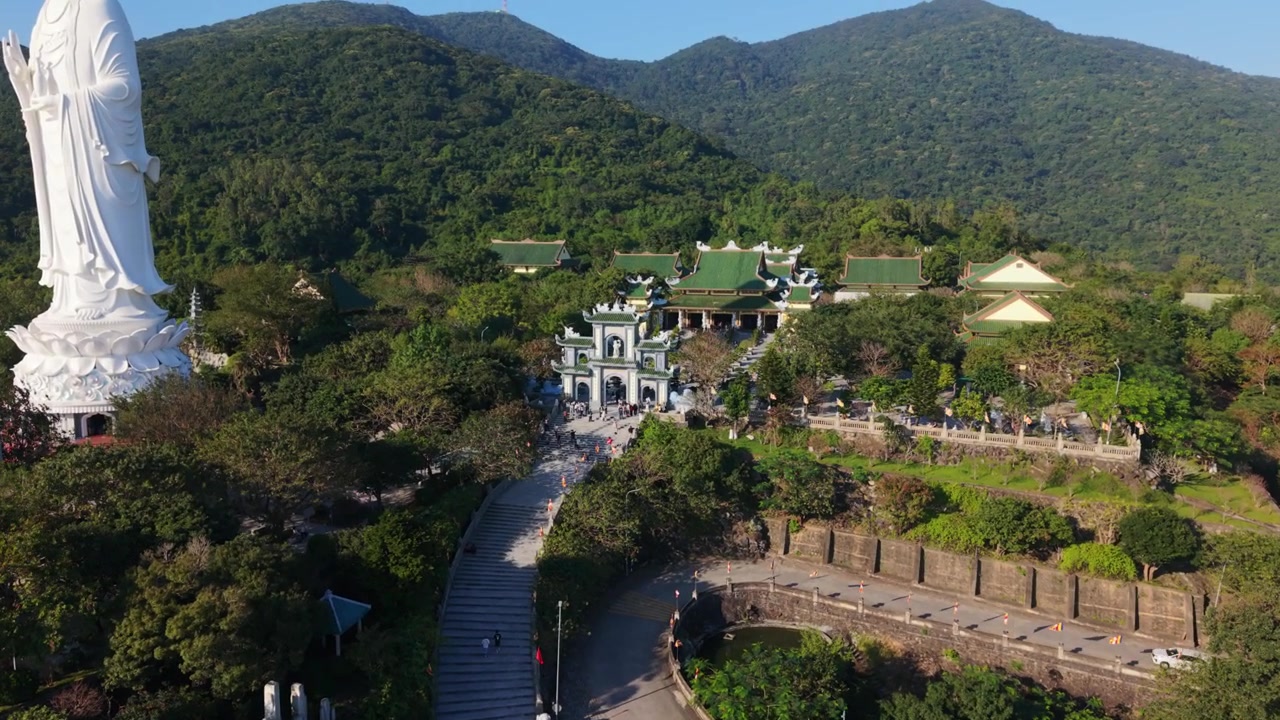 Việt Nam, Đà Nẵng, Tượng Phật Trắng Khổng Lồ nhìn ra đồi tại Chùa Linh Ứng Việt Nam, các nhà sư và Phật tử châu Á leo bậc đá, du khách chụp ảnh nền núi toàn cảnh, mềm mại.