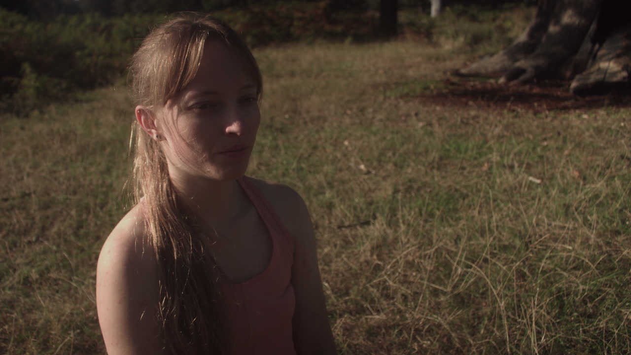 primer plano de una mujer joven sentada en el parque y estirando la espalda para tocar su dedo del pie con la mano