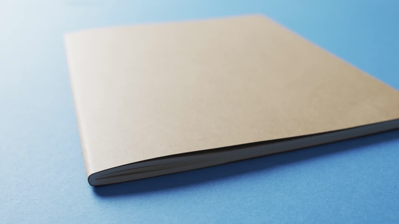 Close up of closed brown book with copy space on blue background in slow motion