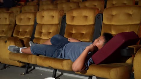 a boy laying down on armchair in cinema.