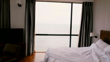 camera zooms in on large modern comfortable hotel apartment window with incredible scenic cloudy ocean waves view.