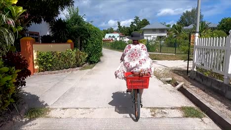 Woman-riding-bicycle-down-narrow-paved-road-in-the-Seychelles-past-fence-and-bushes