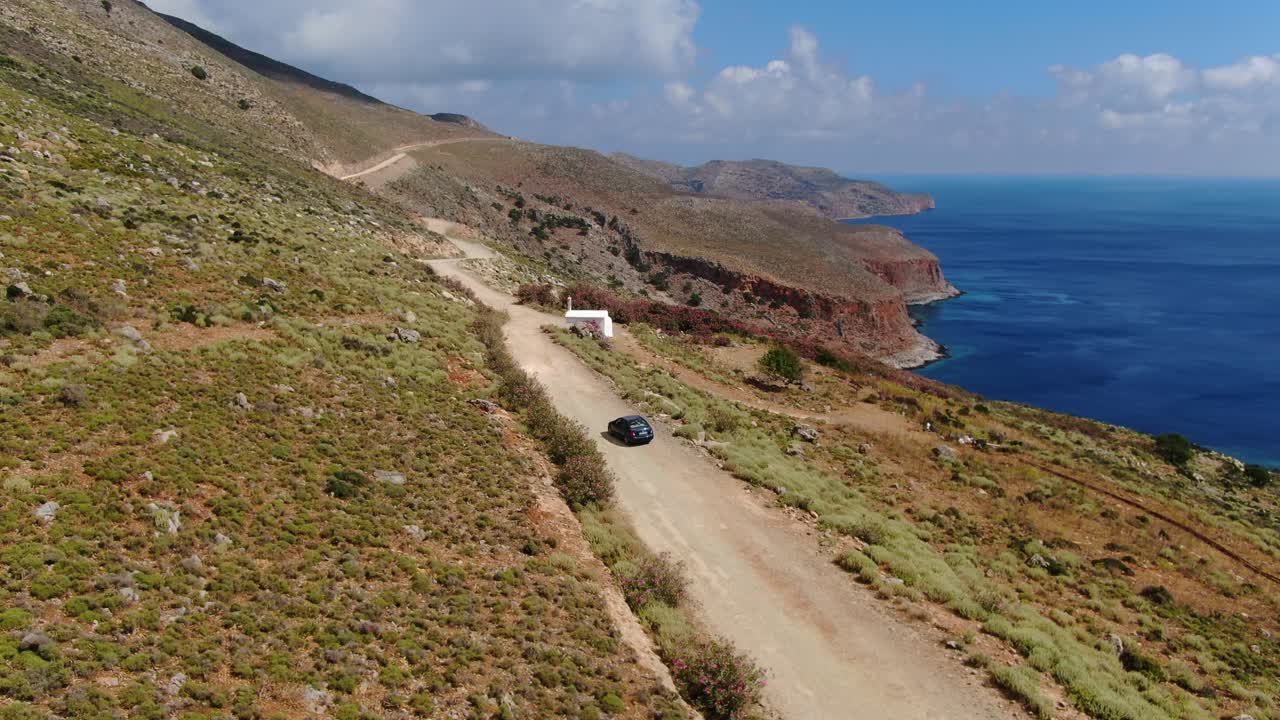 Stopped car in Crete Greece starts advancing along a dirt road near Balos beach, Blurred plates aerial hovering shot