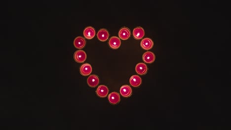 toma aérea de velas rojas encendidas en forma de corazón romántico sobre fondo negro