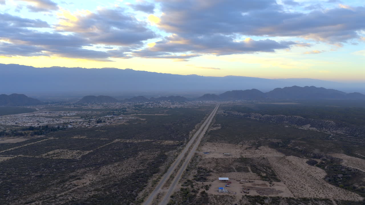 Sunrise over a valley road cutting through on deserted terrain with distant mountains under moody sky, Av. la Mexicana, Chilecito, La Rioja Province, Argentina