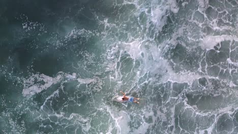 aerial: amazing footage of surfer paddling through strong ocean waves, bird's eye view