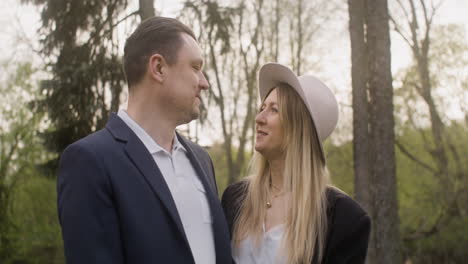 retrato de una pareja elegante que se mira y luego sonríe a la cámara mientras está de pie en el parque