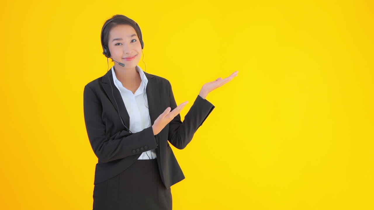 A young businesswoman wearing a headset, headphones, and mic raises her hands to present in the empty space next to her. Copy space