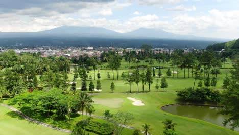 Vibrant-nature-and-cityscape-with-massive-mountain-behind,-aerial-fly-backward-view