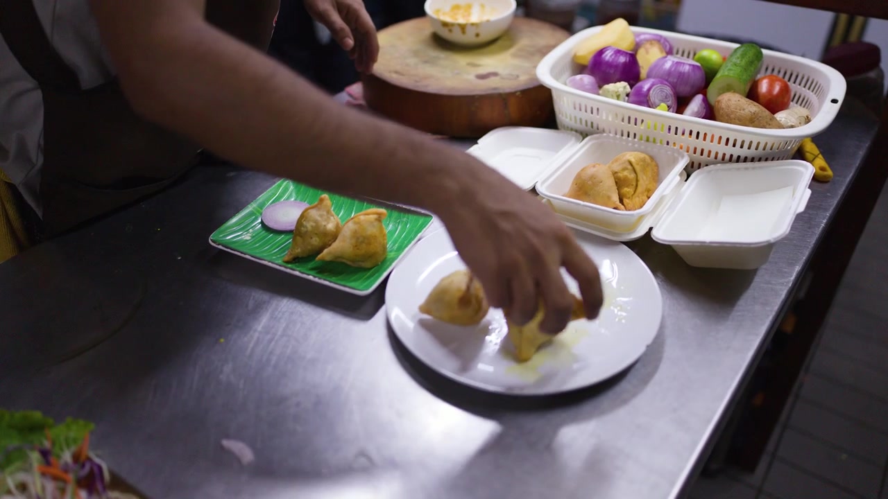 Primo piano di mani che sistemano samosa fritti in contenitori da asporto su un bancone in acciaio inossidabile