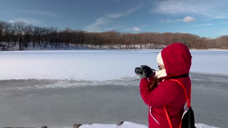 girl using a dslr camera taking photos of a landscape near a frozen lake in winter