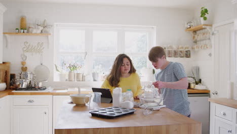 Junges-Down-Syndrom-Paar-Befolgt-Rezept-Auf-Digitalem-Tablet,-Um-Zu-Hause-In-Der-Küche-Kuchen-Zu-Backen