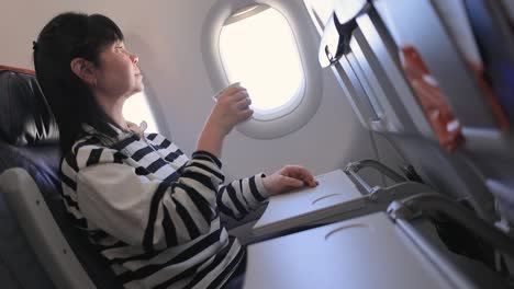 woman sitting inside airplane and looking at window and drinks coffee.