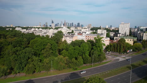 traffic through neighborhood park and warsaw city skyline in distance, aerial