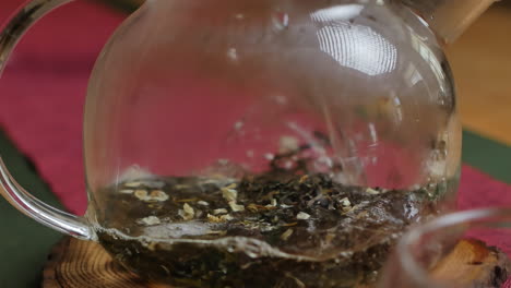 pouring hot water over tea leaves in a glass teapot