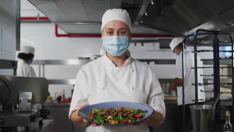 portrait of caucasian female chef wearing face mask presenting dish