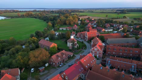 a small village illuminated by golden hour light, casting long shadows over the surrounding fields. fantastic aerial view flight circle drone footage
