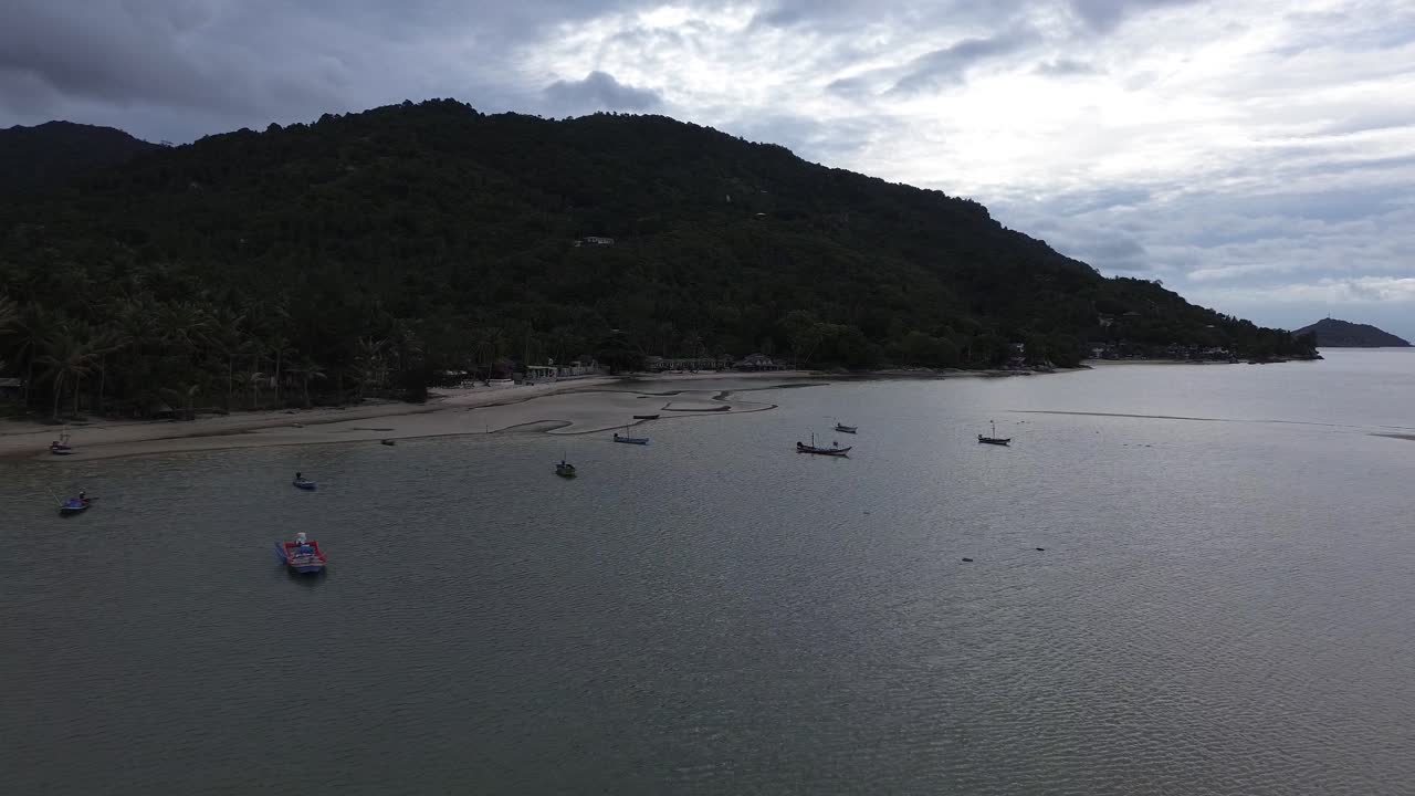 Aerial view of traditional fishing boats floating near Koh Phangan, Thailand, with lush tropical hills, palm trees and green mountains forming a scenic backdrop