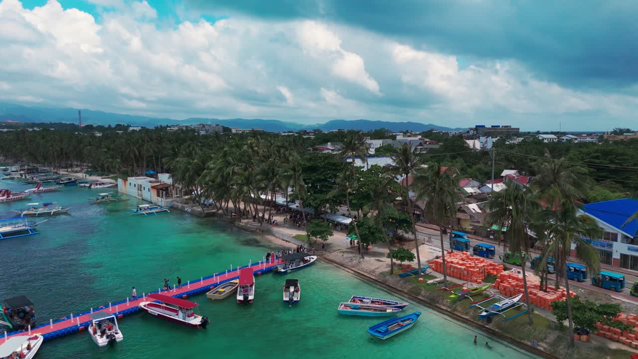 Vibrant 4K drone footage of Boracay jetty with colorful boats, palm-lined shore, and turquoise waters in the Philippines—ideal for travel, tourism, and tropical destination media